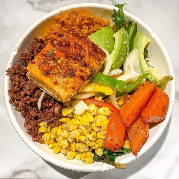 A vibrant bowl with spicy salmon, red rice, yellow rice, avocado, corn, carrots, and peppers.