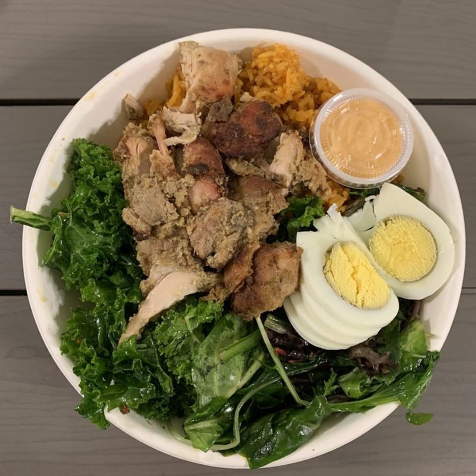 A bowl of African cuisine with chicken, rice, kale, spinach, hard-boiled eggs, and sauce.
