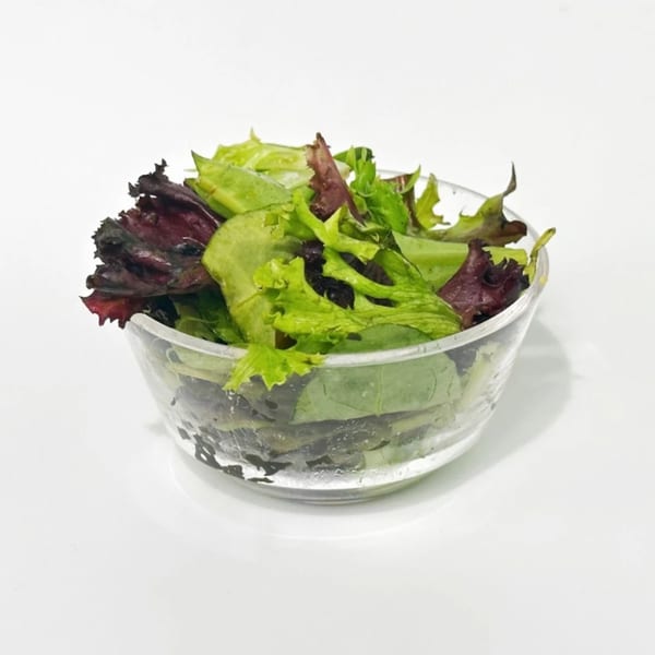 Fresh mixed greens, including red and green lettuce, in a clear glass bowl on a white surface.