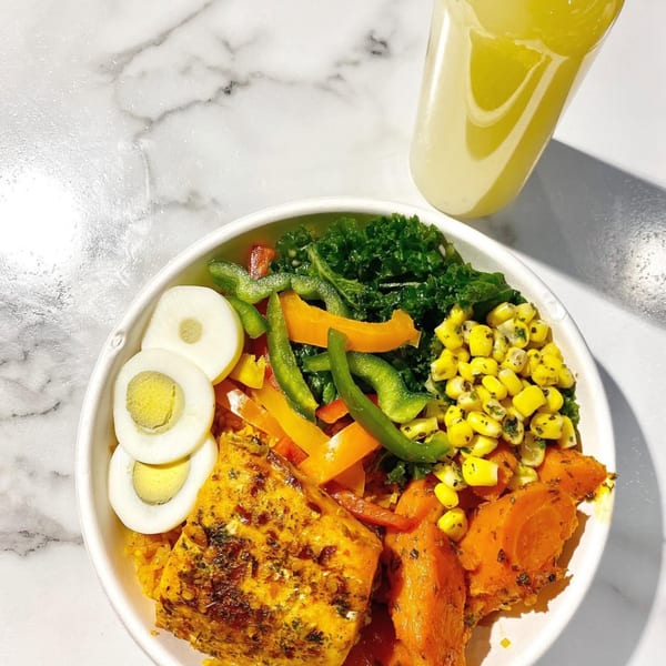 A vibrant African bowl with salmon, sweet potatoes, kale, corn, bell peppers, and hard-boiled eggs.