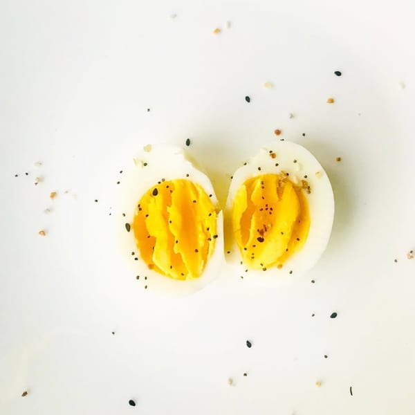 Two hard-boiled egg halves, sprinkled with black pepper and other spices, on a white background.