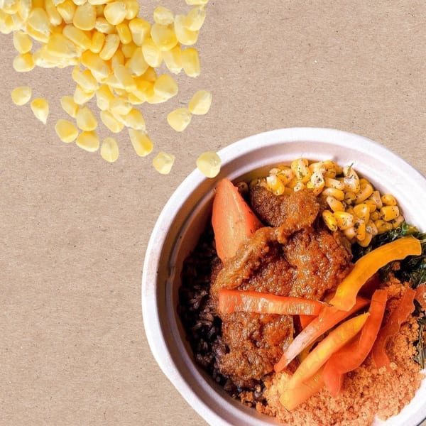 African dish with meat, black rice, corn, and vegetables in a bowl, with loose corn kernels.