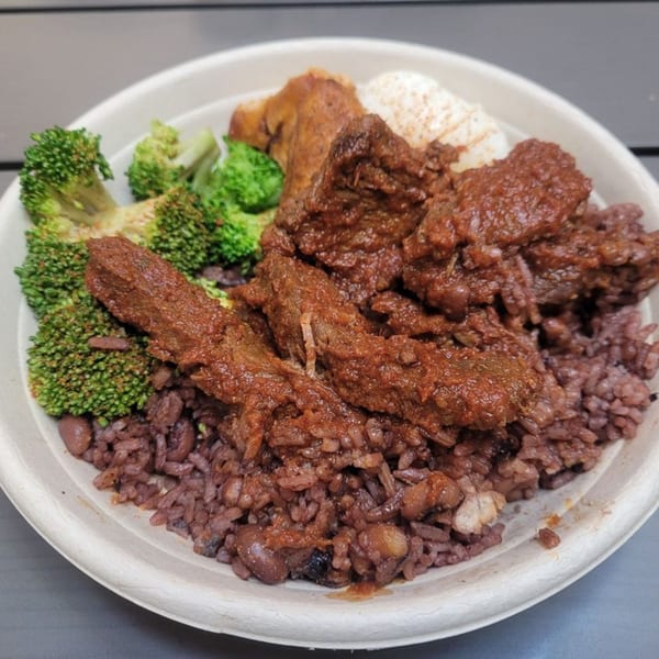 A bowl of ākra Eatery's African cuisine featuring stewed meat, rice and beans, and broccoli.
