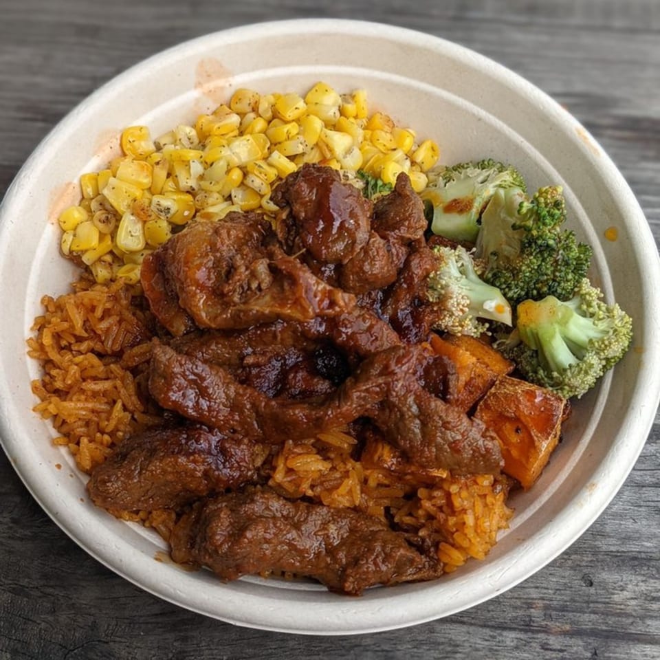 A bowl of African cuisine with meat, rice, corn, broccoli, and sweet potatoes.