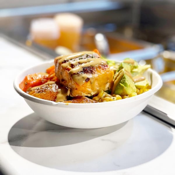 A bowl of African cuisine with salmon, plantains, and vegetables drizzled with sauce.