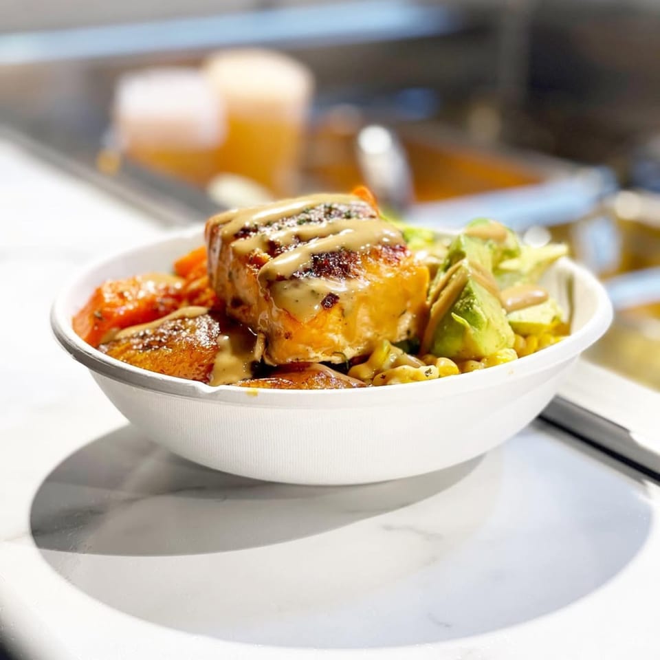 A bowl of African cuisine with salmon, plantains, and vegetables drizzled with sauce.